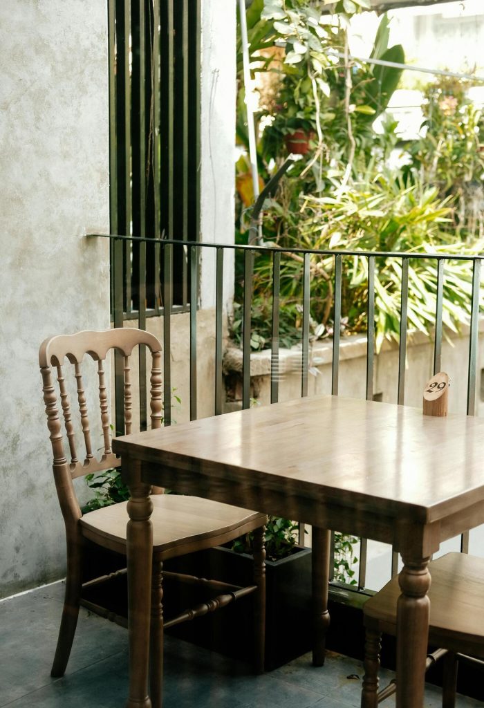 כיסאות ושולחן ניצבים ליד מעקה של מרפסת כשברקע צימחייה שופעת